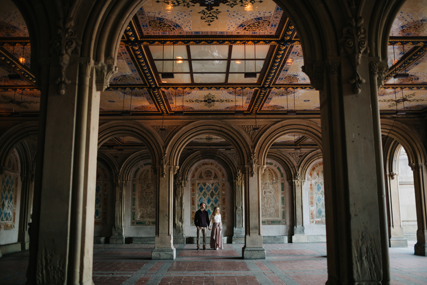 Stylish couple standing under Bethesda Terrace for their fall engagement session in Central Park in New York City