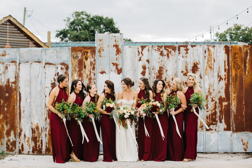 Bride laughing with her bridesmaids wearing crimson backless dresses