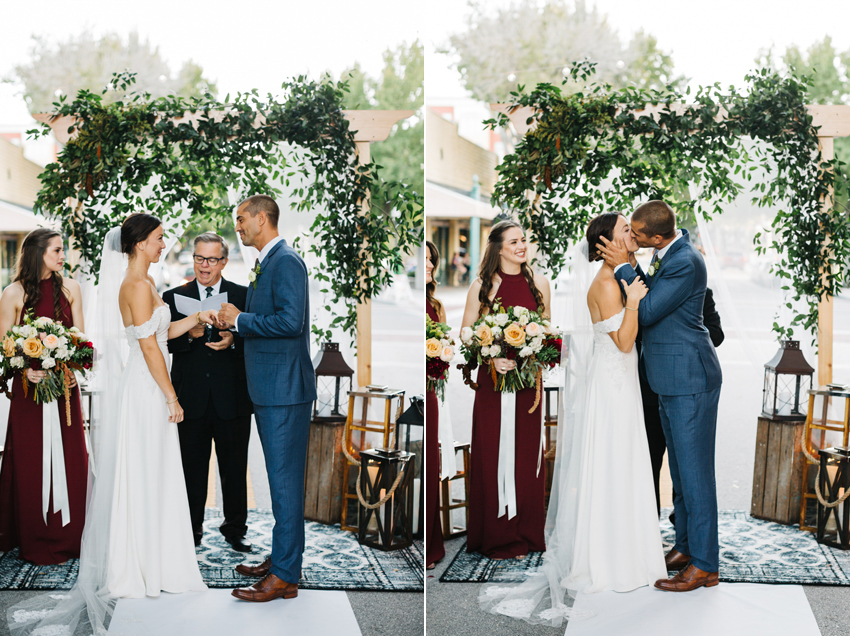 bride and groom kissing under a greenery covered wood arch during their modern ceremony in the street of downtown Lakeland Kentucky Avenue
