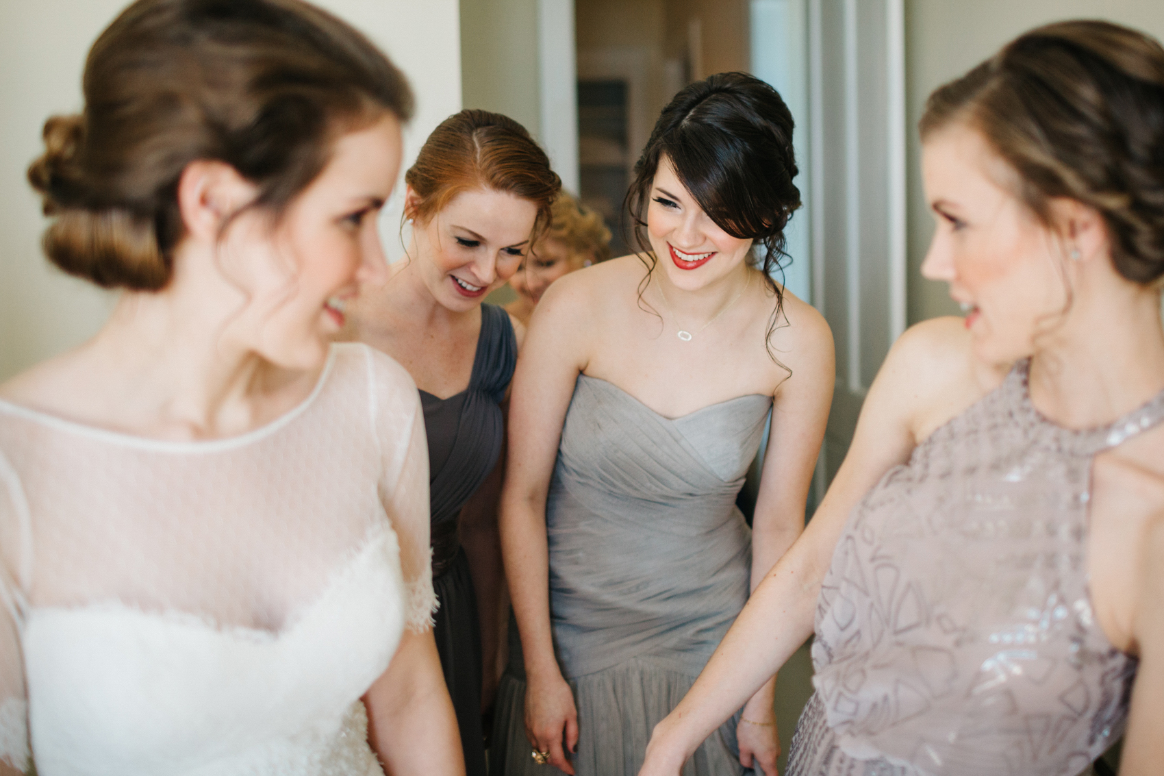 bridesmaids wearing mismatch grey dresses helping the bride get ready