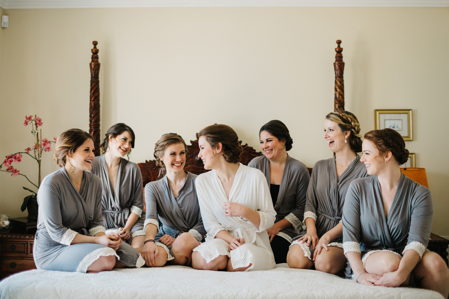 bride and her bridesmaids wearing their robes and sitting on the bed laughing