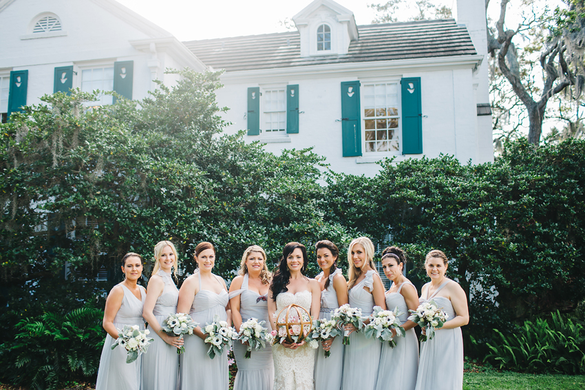 Bridesmaids wearing Amsale dove grey dresses laughing in front of Marie Selby Gardens mansion in Sarasota, Florida