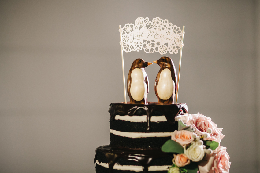 Cute penguin cake topper on romantic chocolate naked wedding cake with fresh flowers