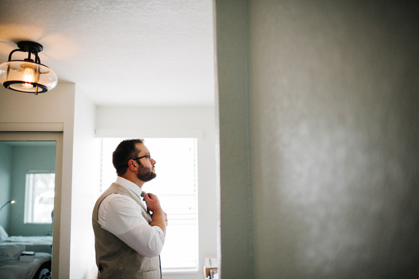Groom fixing his tie in the courtyard suite before the ceremony on the beach at The Posctard Inn