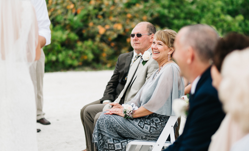 Mother of the bride smiling as she watches the newlyweds say I do at the beach ceremony