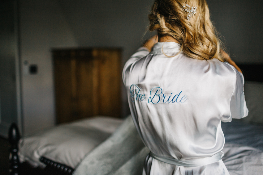 Bride wearing a silk white bridal robe with baby blue lettering on the morning of the wedding