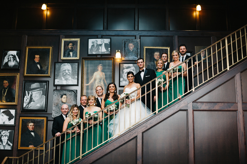 Bridal party photos on the grand staircase at the Oxford Exchange with bridesmaids wearing emerald green dresses and groomsmen wearing black classic tuxes