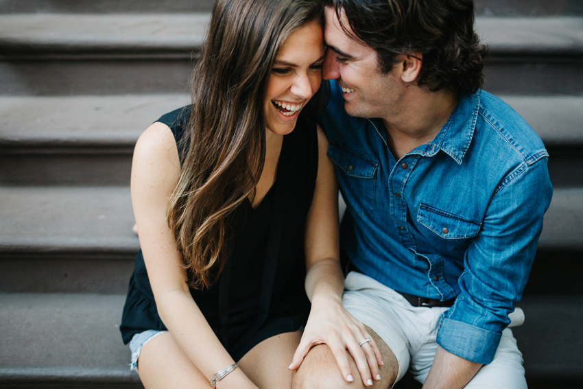 Candid romantic engagement photography of a couple laughing on a stoop in the West VIllage