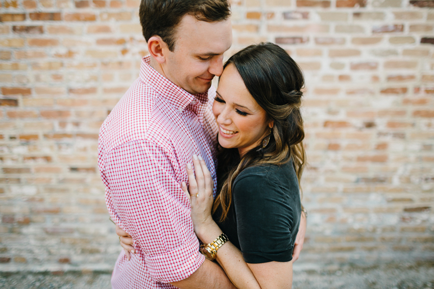 Cute couple laughing during their lifestyle engagement session in front of a brick wall by Tampa Wedding Photographer