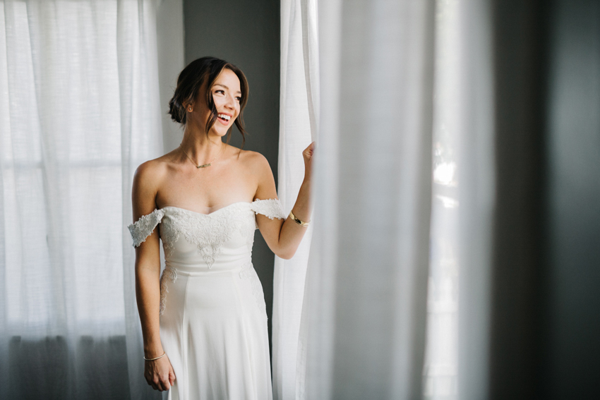 bride wearing a customized lace reformation wedding dress laughing out the window