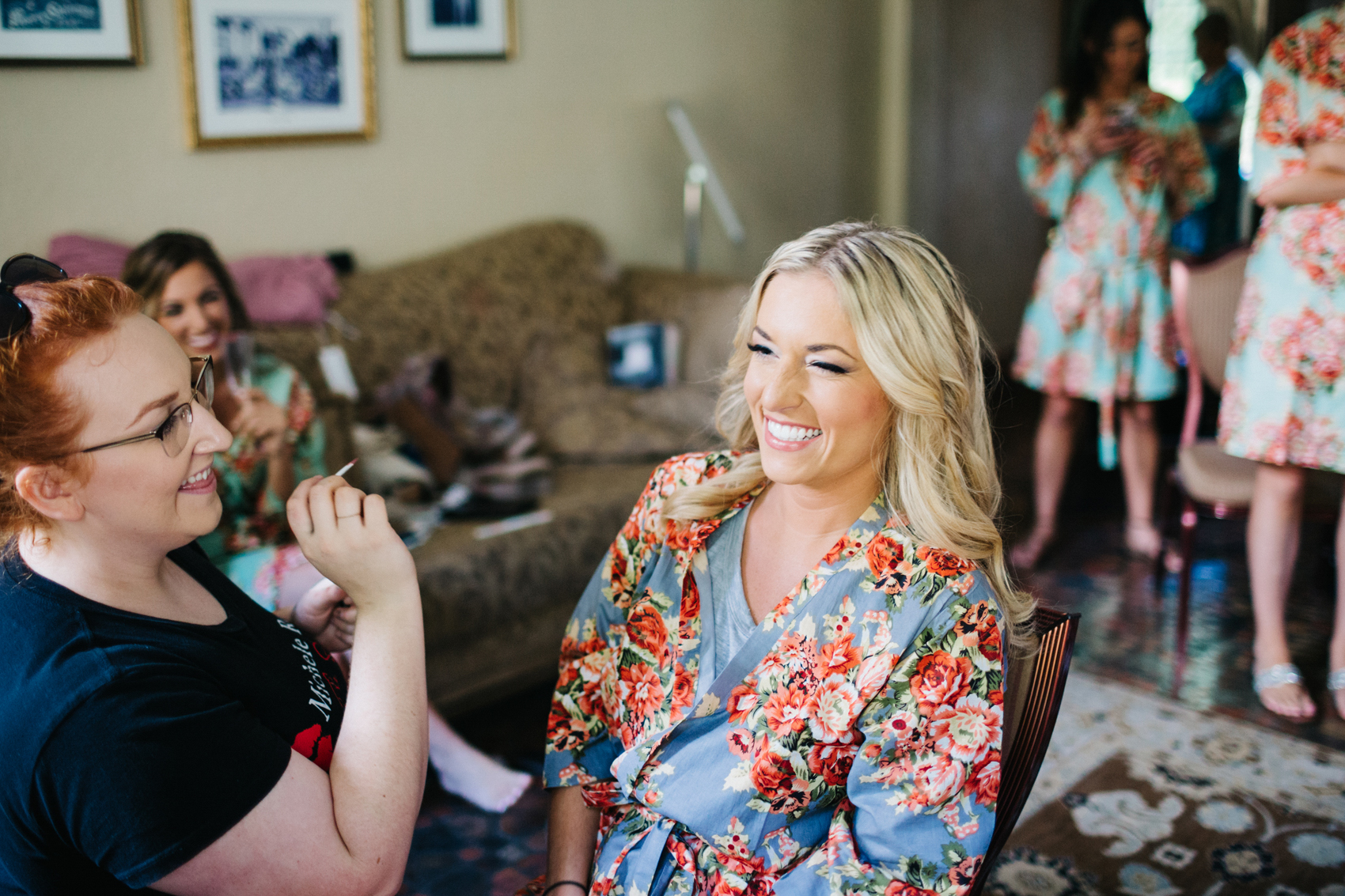 bridesmaid wearing a silk floral robe while she gets her makeup done before the wedding