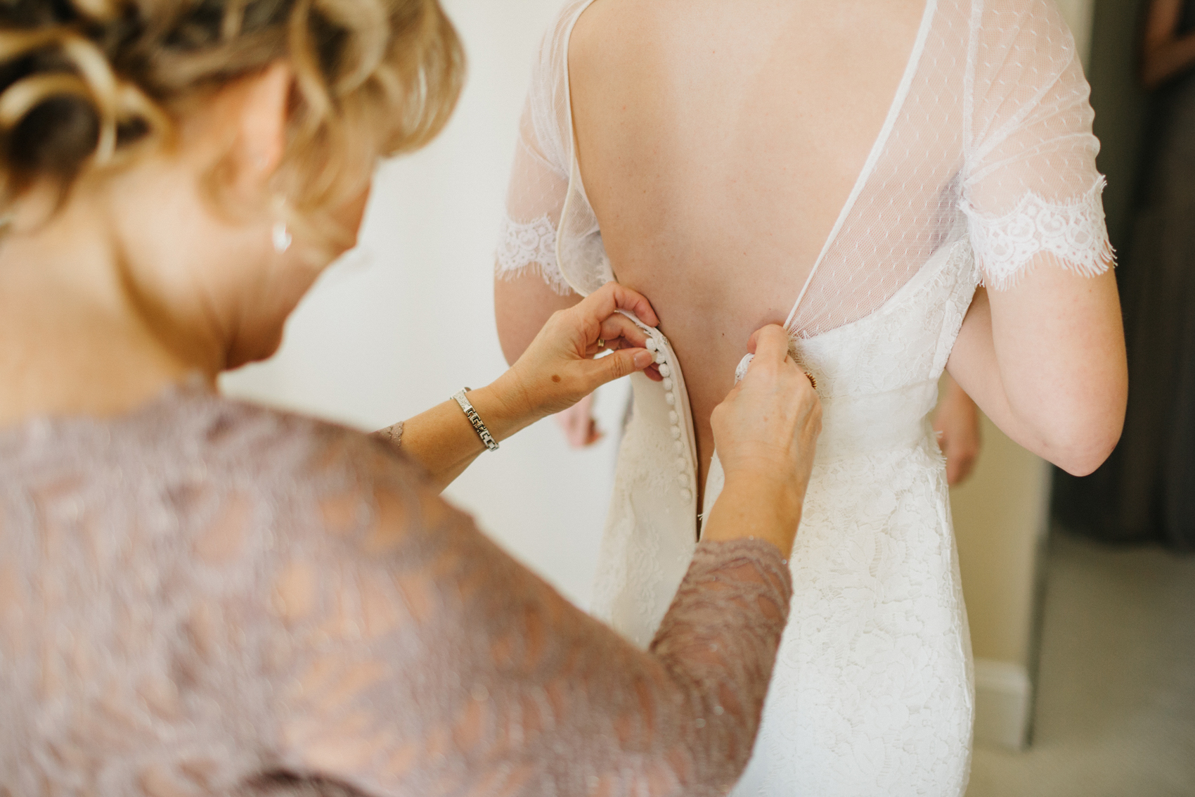 mother of the bride wearing a lavendar lace dress helping the bride get ready