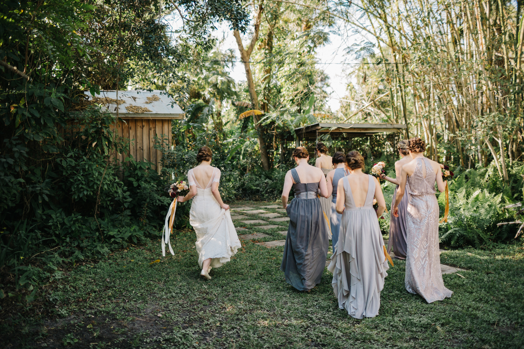 Bride and her bridesmaids wearing mismatched grey dresses walking through the garden