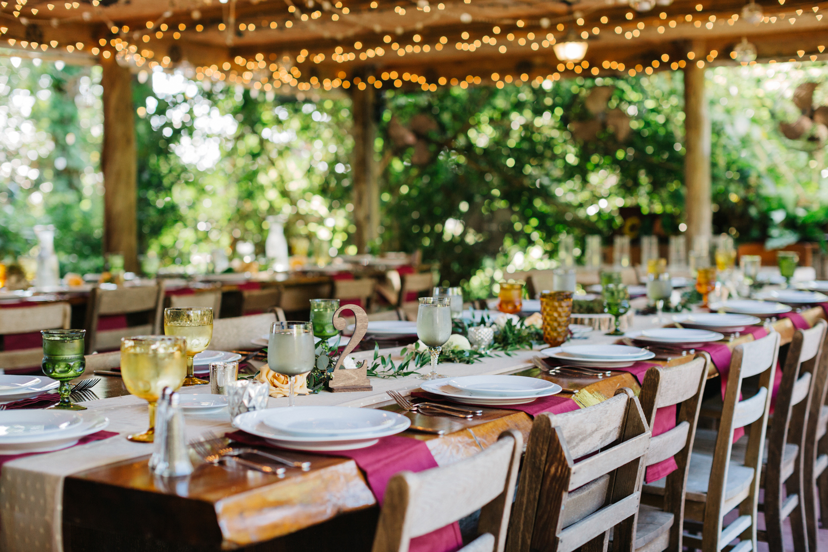 Vintage farm tables, string lights, mismatched goblets, and burgundy linen napkins for the Orlando boho garden reception outdoors