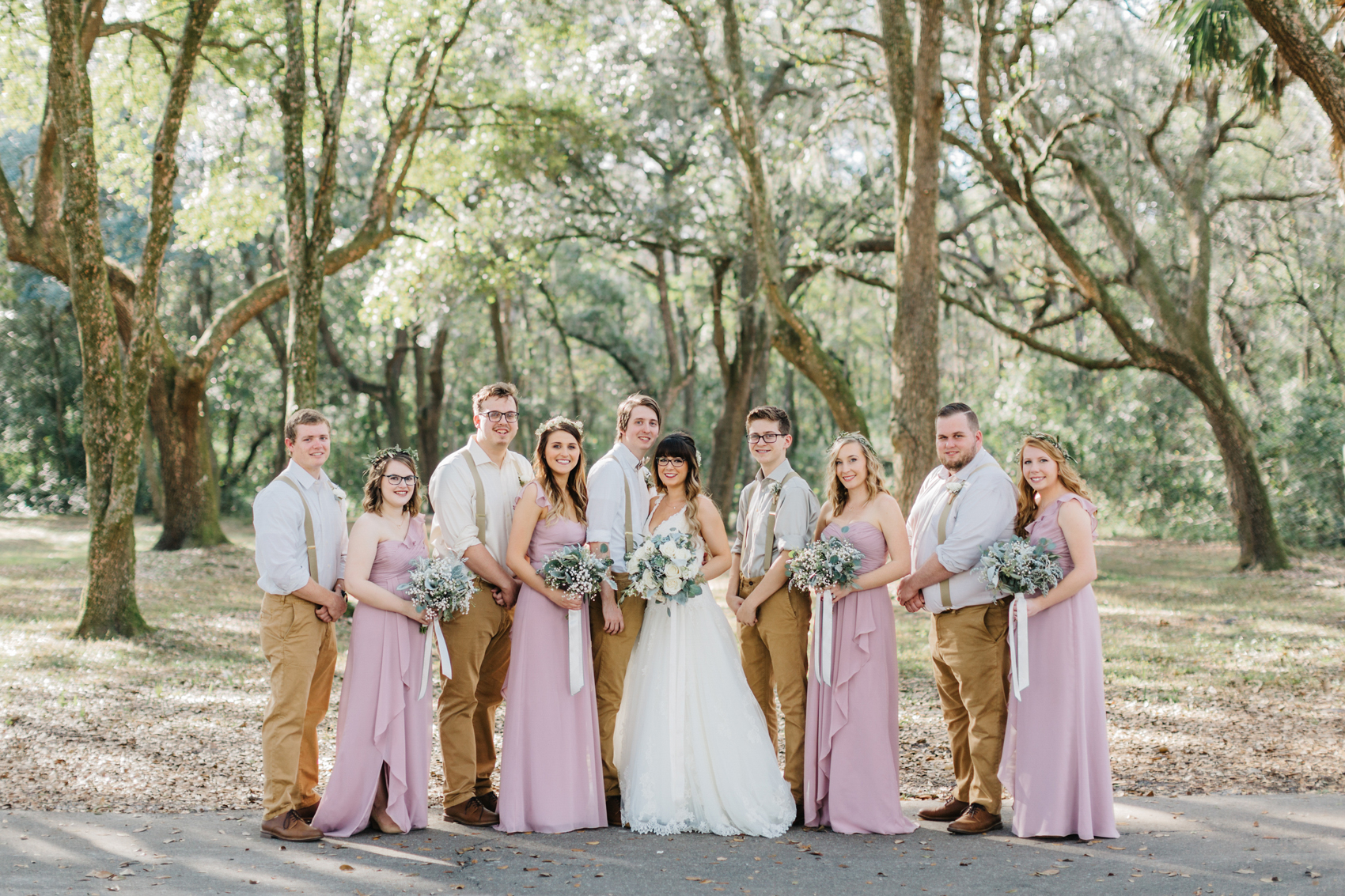 bridesmaids wearing dusty rose gowns and groomsmen wearing khaki pants with suspenders and bowties