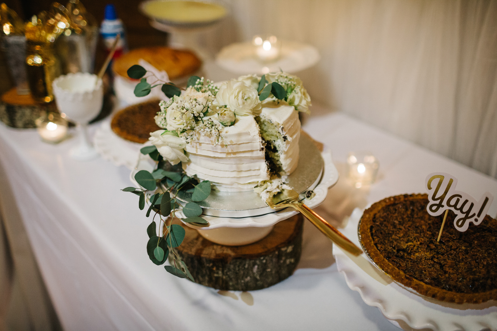 a simple buttercream wedding cake with fresh flowers and greenery with a tree stump cake stand