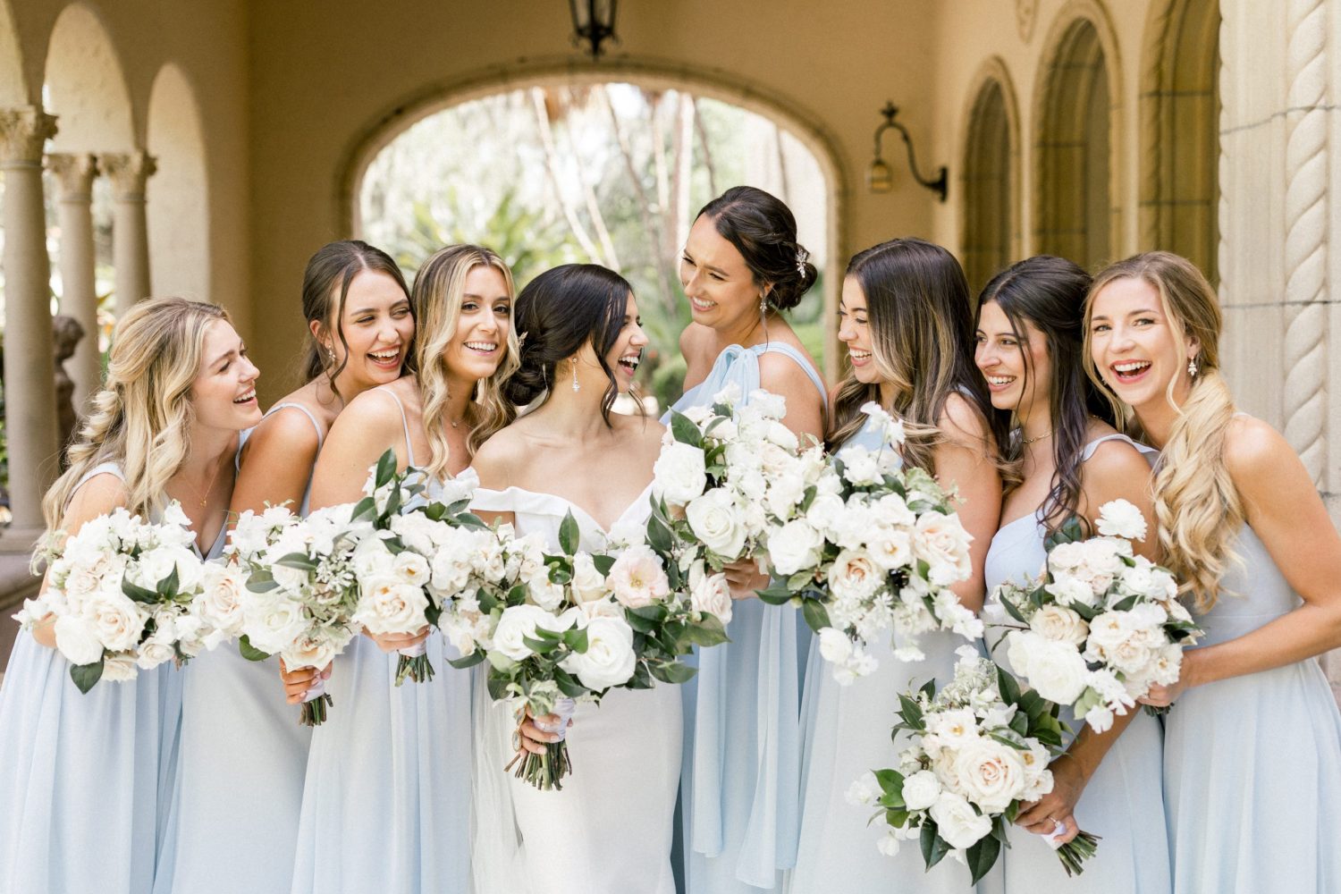 bridesmaids wearing dusty blue dresses laughing outside of the towel Crowley estate with neutral lush blooms