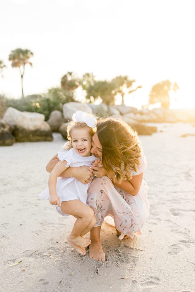 mom kissing baby girl during sunset at the beach