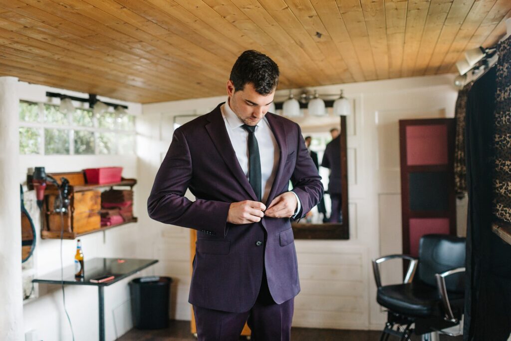 groom buttoning his purple suit jacket