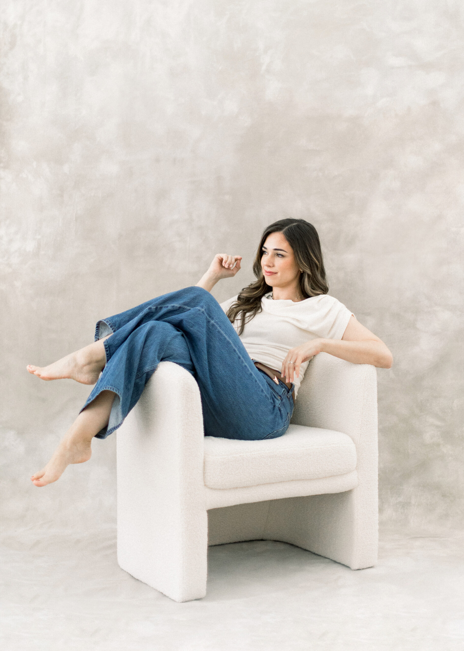 Tampa family photographer sitting on a white chair posing in front of a hand painted canvas backdrop